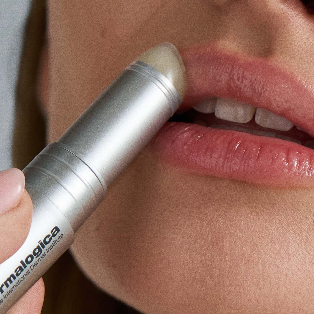 Person applying a lip balm stick to their lips with a focus on the brand 'dermalogica'. 