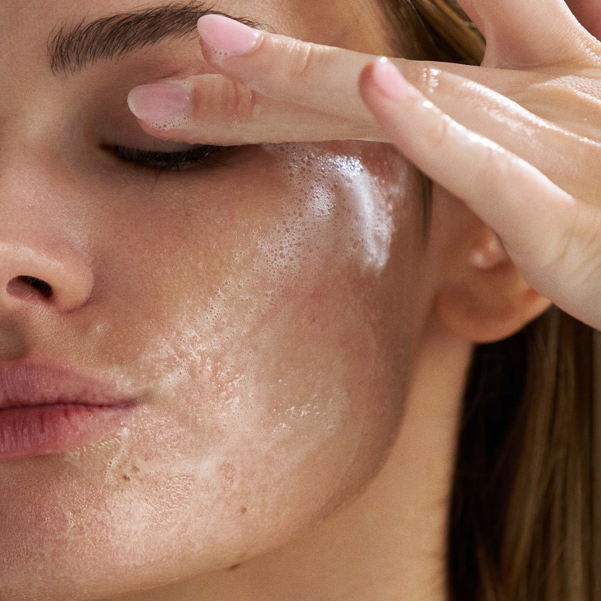 Close-up of a person applying a cleanser to their face. 